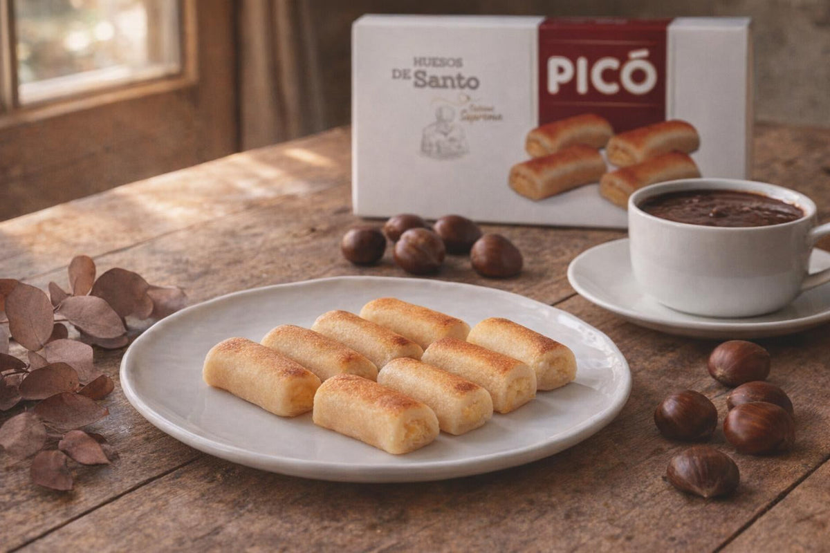 Huesos de santo en un plato con chocolate caliente y castañas, y la caja de Huesos de Santo Picó al fondo