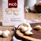 Almendras rellenas de turrón sobre una tabla de madera, junto a su caja Picó