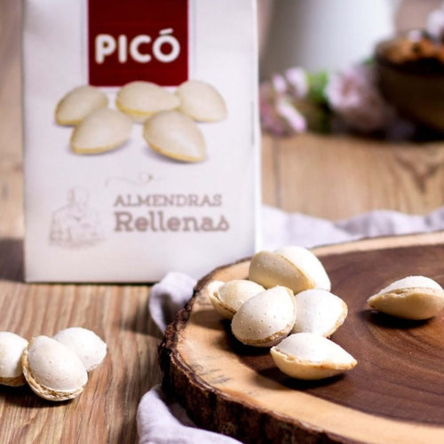 Almendras rellenas de turrón sobre una tabla de madera, junto a su caja Picó