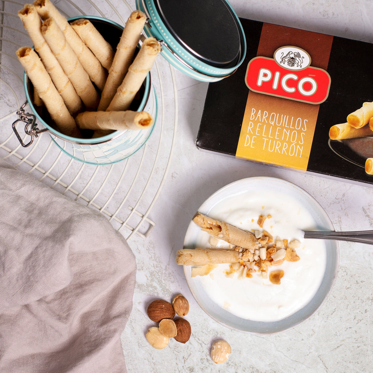Barquillos rellenos de turrón en un bote de cristal, con yogur y almendras, junto a la caja Picó
