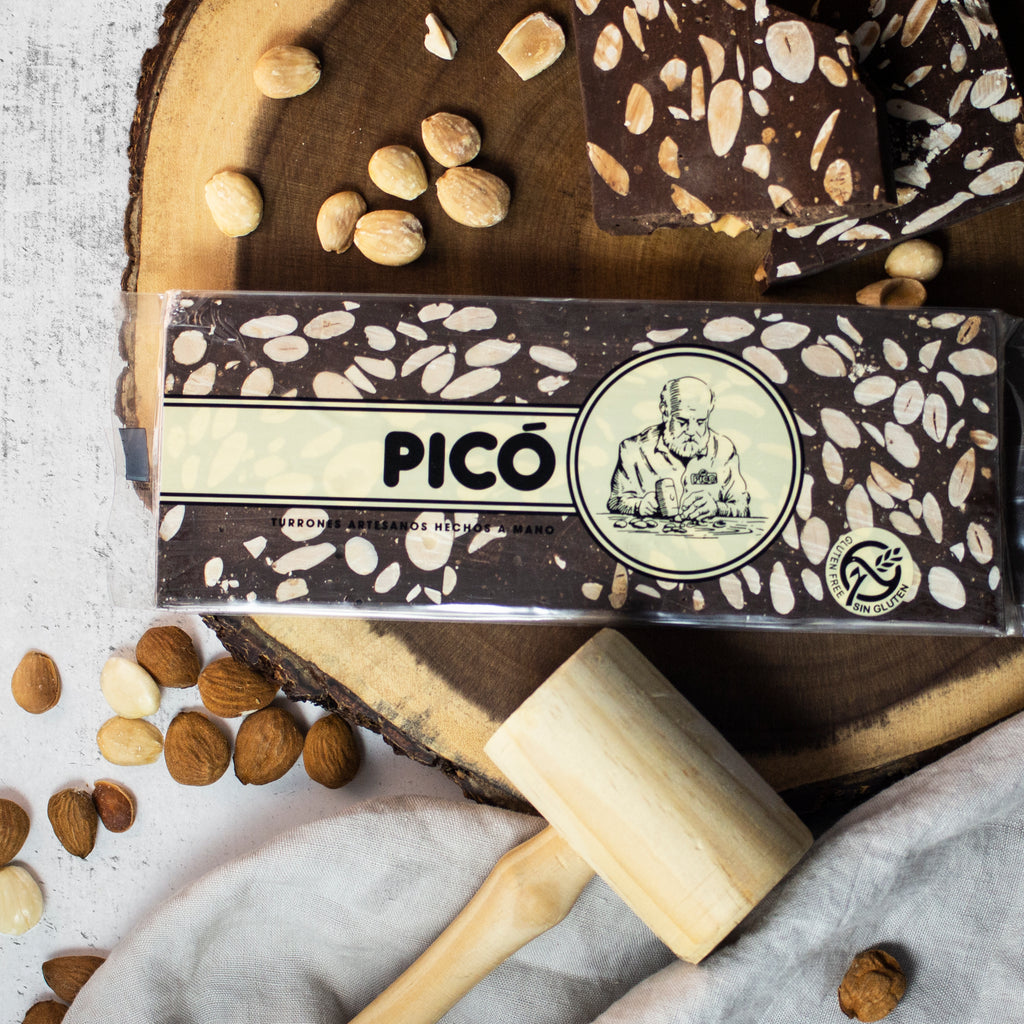 Turrón de chocolate negro con almendras hecho a mano sobre una rodaja de madera, con mazo y almendras