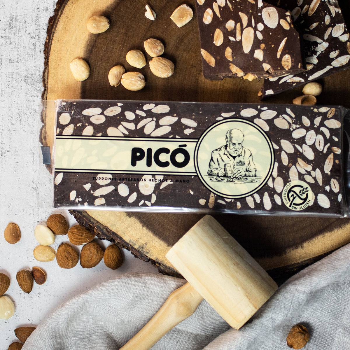 Turrón de chocolate negro con almendras hecho a mano sobre una rodaja de madera, con mazo y almendras