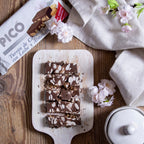 Turrón de chocolate con leche y almendras sin azúcar cortado en porciones sobre una tabla, con flores de almendro