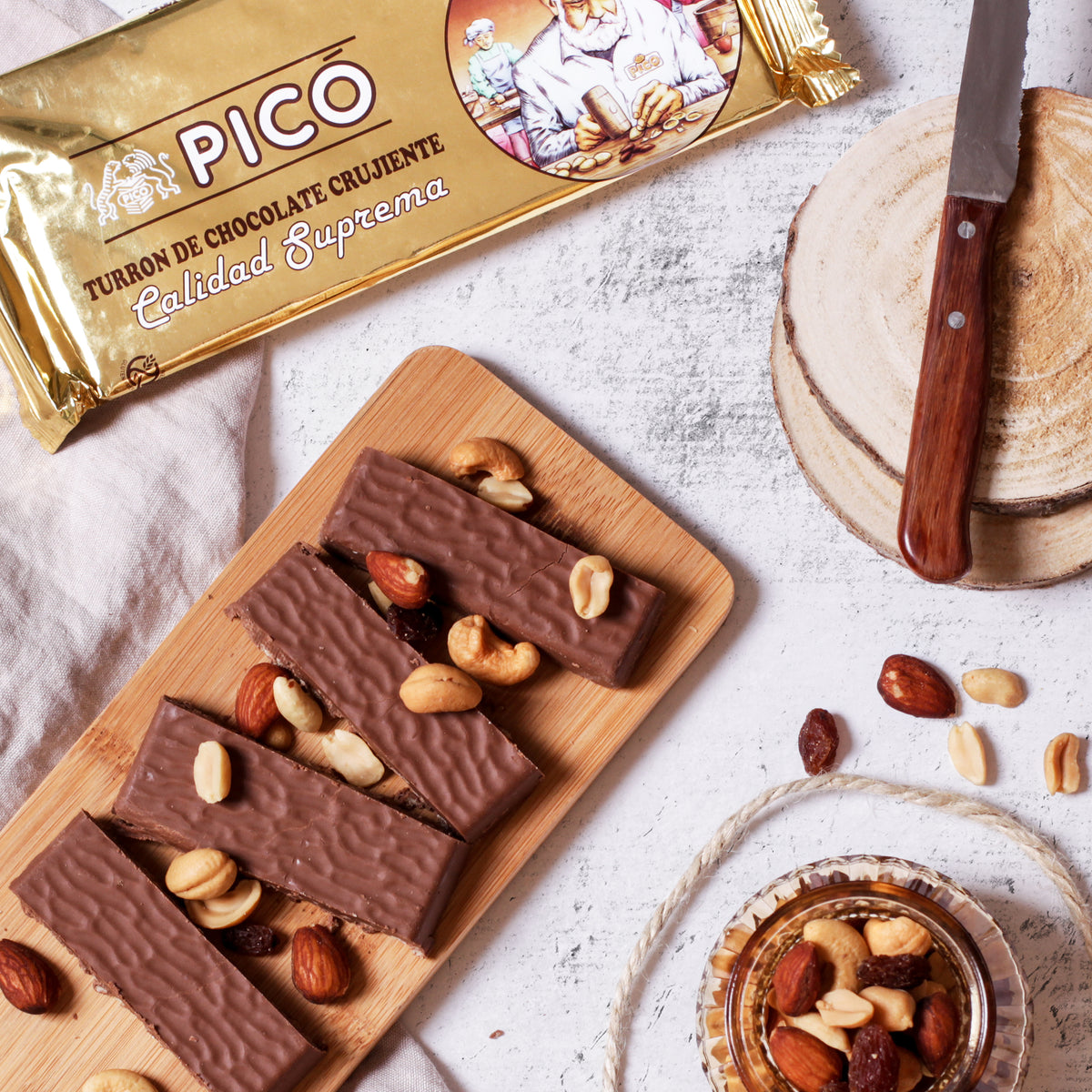 Barritas de turrón de chocolate crujiente sobre una tabla, con frutos secos y su envase Picó