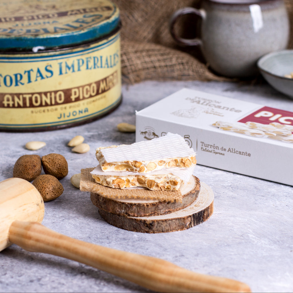 Turrón de Alicante partido sobre rodajas de madera junto a una lata antigua de Tortas Imperiales Antonio Picó