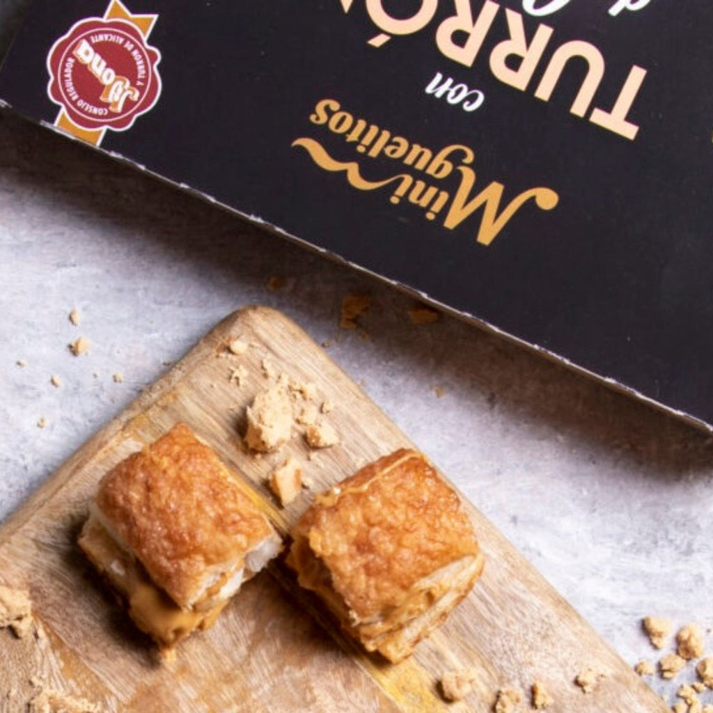 Mini miguelitos de hojaldre rellenos de turrón de Jijona sobre una tabla, con la caja detrás