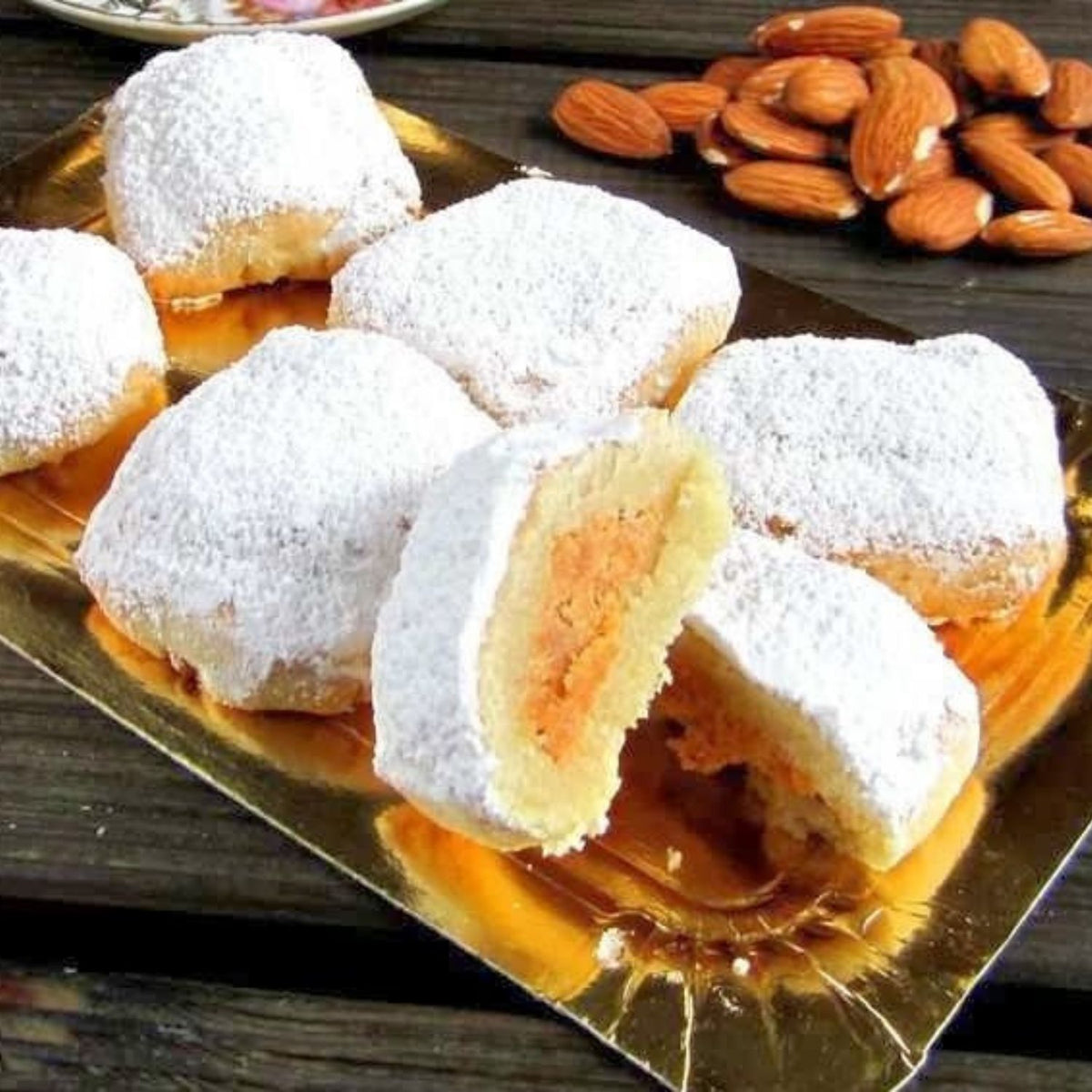Pasteles de yema con azúcar glas, uno partido por la mitad, con almendras al lado