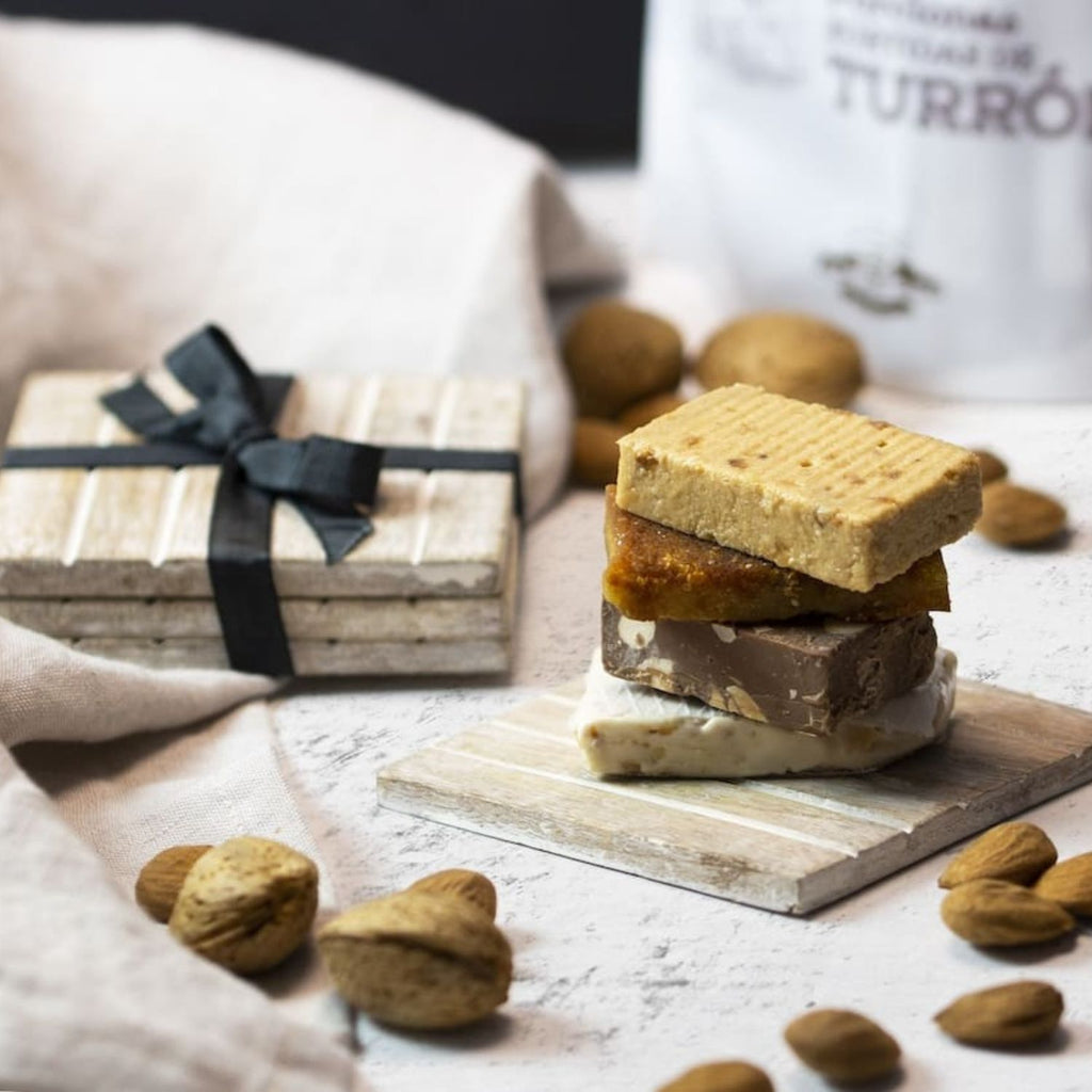 Porciones de turrón surtidas apiladas junto a un paquete de regalo y almendras