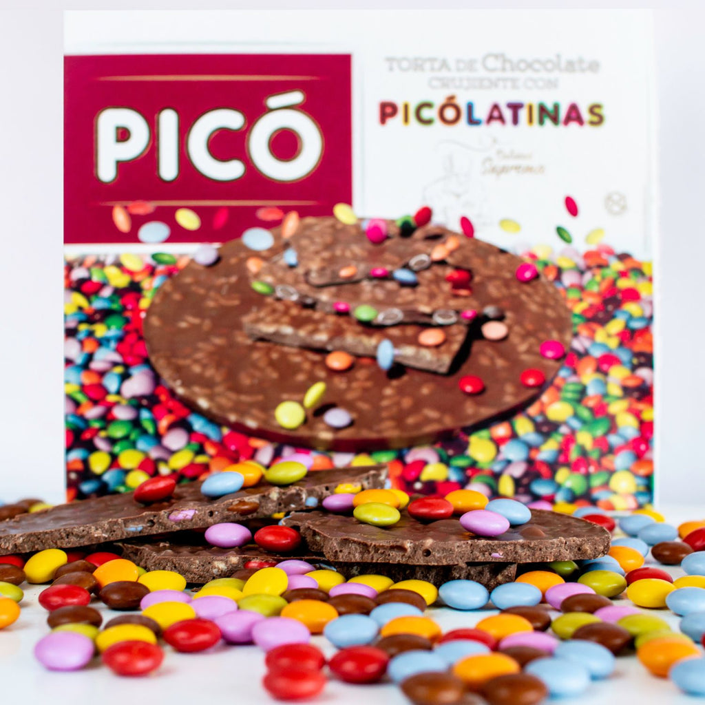Torta de chocolate crujiente con Picolatinas de colores partida sobre un lecho de grageas, con la caja Picó