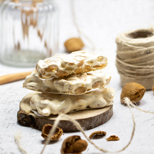 Trozos de turrón de Alicante apilados sobre una rodaja de madera, con almendras
