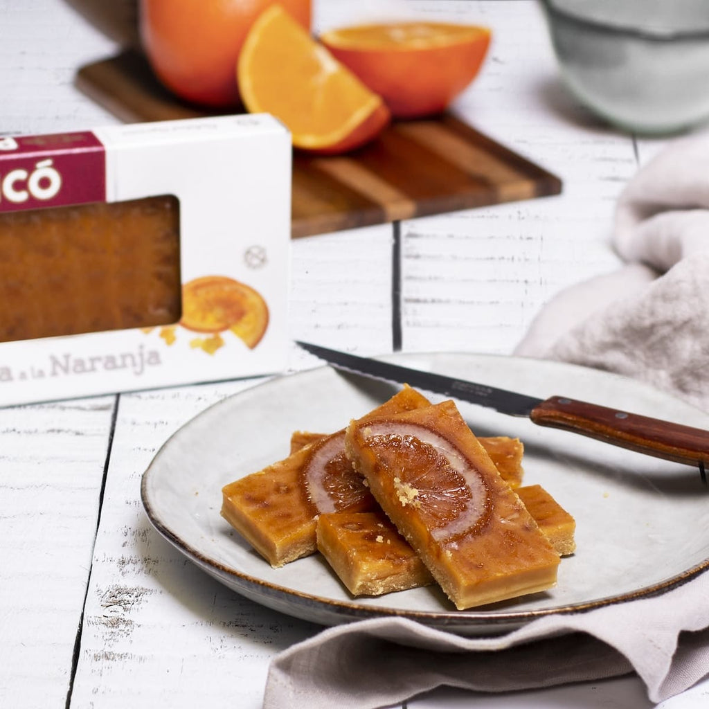 Barritas de turrón de yema a la naranja en un plato, con naranjas y la caja Picó
