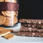 Trozos de turrón de chocolate crujiente con galleta María apilados junto a galletas