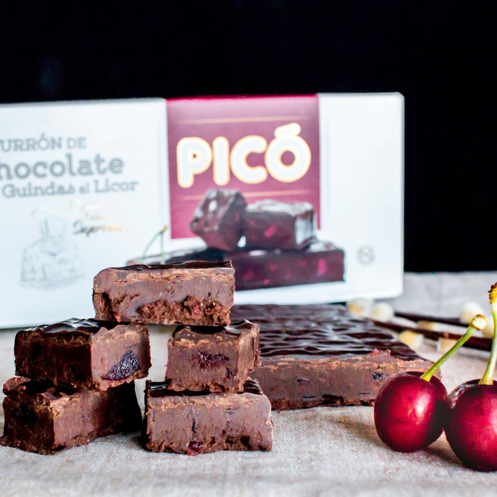 Bloques de turrón de chocolate con guindas al licor apilados, con cerezas y la caja Picó detrás