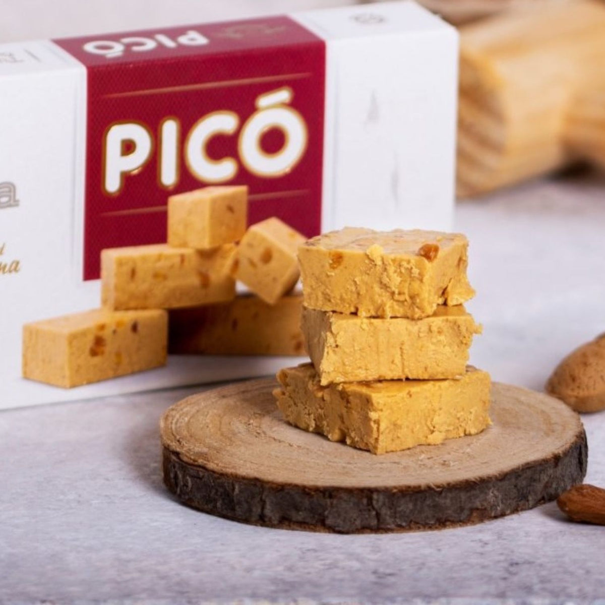 Dados de turrón de Jijona apilados sobre una rodaja de madera, con la caja Picó detrás