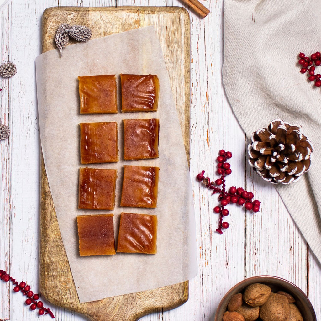 Porciones de turrón de yema tostada sin azúcar sobre papel de horno en una tabla, con piñas