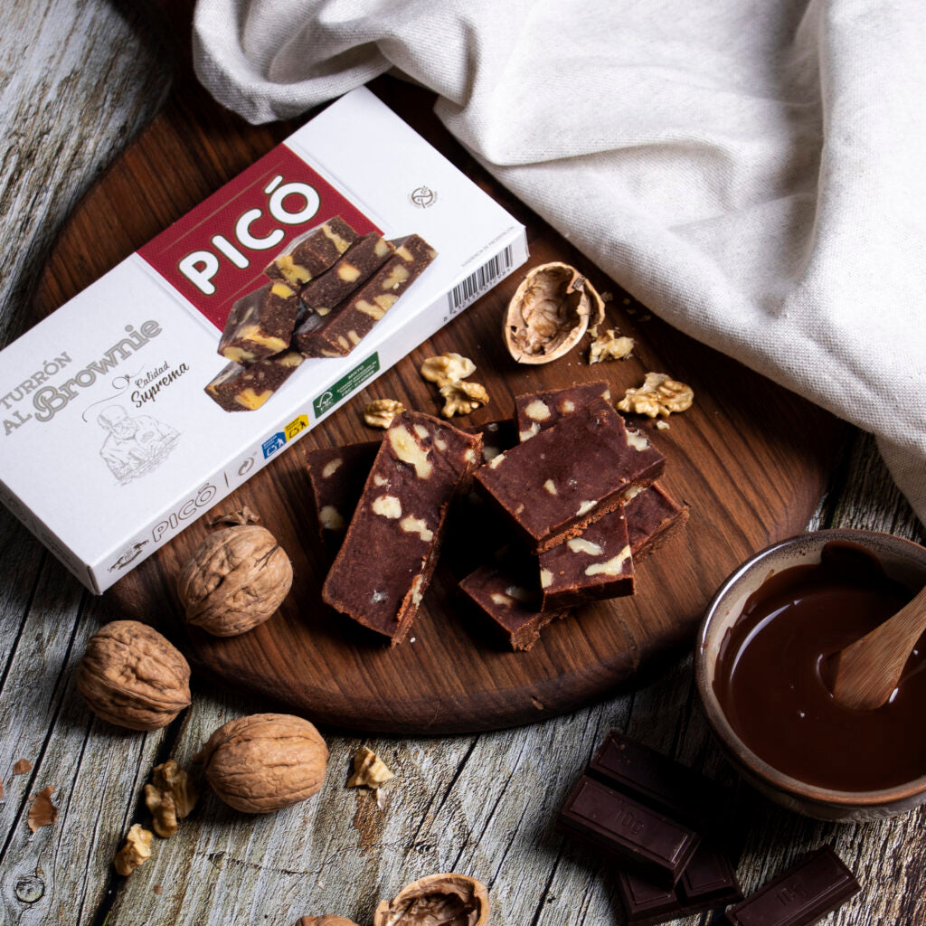 Turrón de mazapán al brownie cortado sobre una tabla, con nueces, chocolate fundido y su caja Picó