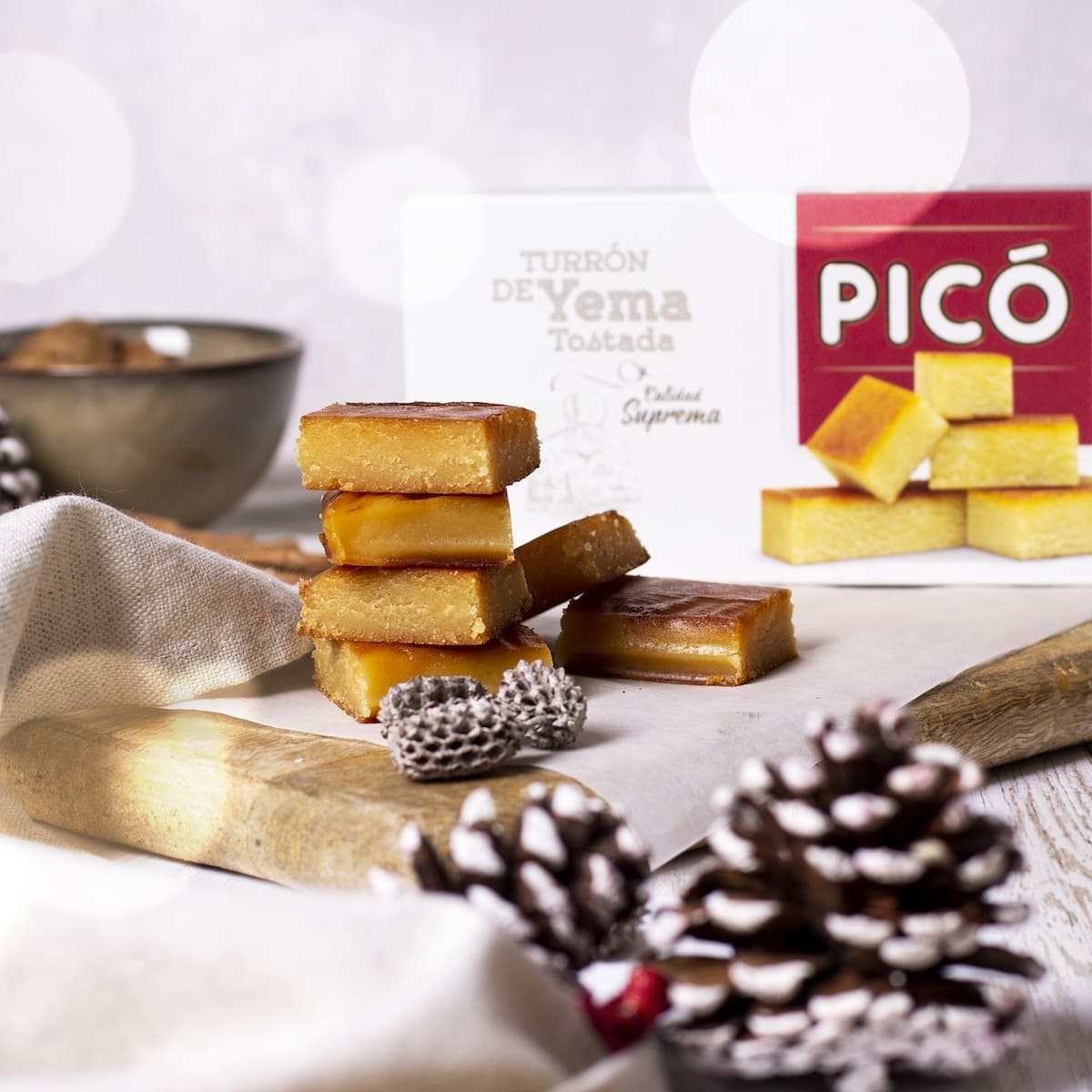 Dados de turrón de yema tostada apilados con piñas, con la caja Picó detrás