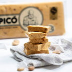 Porciones de turrón de Jijona hecho a mano apiladas sobre un paño, con la tableta Picó detrás